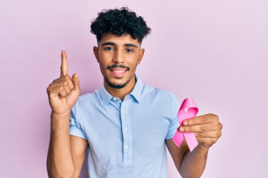 Genç Arap yakışıklı adam elinde pembe kanser kurdelesi ile gülümsüyor bir fikirle ya da soru işareti ile mutlu bir yüzle, bir numara 