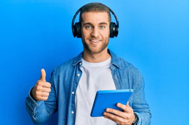 Kulaklık takan, mutlu ve olumlu gülümseyen, başparmağıyla mükemmel ve onay işareti yapan genç beyaz bir adam. 