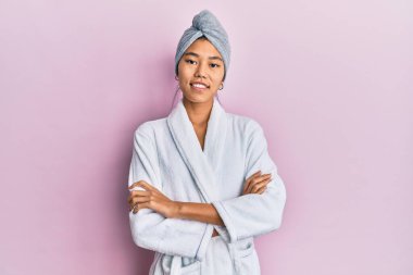 Duş havlusu şapkası ve bornoz giymiş kollarını kavuşturup kameraya gülümseyen genç Çinli kadın. pozitif kişi. 