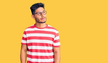 Yakışıklı Latin Amerikalı genç adam günlük kıyafetler ve gözlük takıyor gülümsüyor ve yan tarafa bakıyor ve düşünüyor.. 