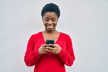 Genç Afrikalı Amerikalı kadın şehirde akıllı telefon kullanarak mutlu bir şekilde gülümsüyor..