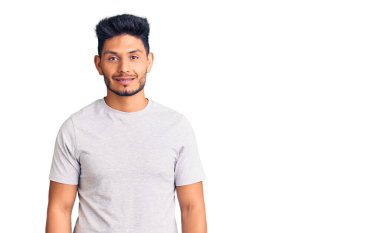 Yakışıklı Latin Amerikalı genç adam mutlu ve havalı bir gülümsemesi olan sıradan bir tişört giyiyor. şanslı kişi. 