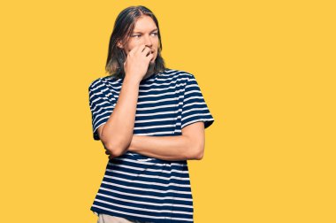 Uzun saçlı, sıradan çizgili tişört giyen yakışıklı beyaz bir adam. Ağzı tırnak yiyen elleri yüzünden gergin ve stresli görünüyor. anksiyete. 