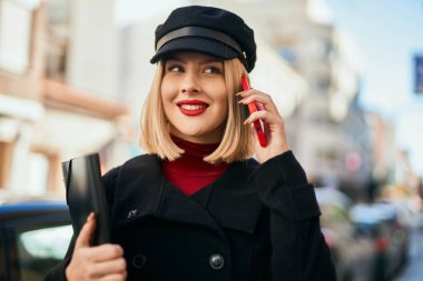 Genç sarışın kadın gülümsüyor. Şehirdeki akıllı telefondan konuşuyor..