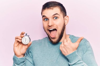 Kronometreyi tutan yakışıklı genç adam baş parmağını yana kaldırıyor ve ağzı açık gülümsüyor. 