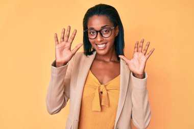 Genç Afro-Amerikan kadın iş kıyafetleri giyip on numarayı gösterip işaret ederken kendinden emin ve mutlu bir şekilde gülümsüyor.. 