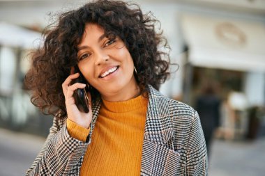 Genç İspanyol iş kadını gülümsüyor. Şehirdeki akıllı telefondan mutlu bir şekilde konuşuyor..