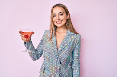 Genç ve güzel sarışın kadın alkollü tropikal kokteyl içiyor. Pozitif ve mutlu görünüyor. Kendine güvenen bir gülümsemeyle dişlerini gösteriyor. 