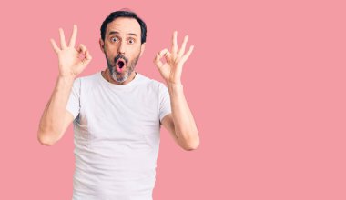 Gündelik tişört giyen orta yaşlı yakışıklı adam şaşırmış ve şok olmuş bir şekilde parmaklarıyla onay sembolü yapıyor. çılgın ifade 