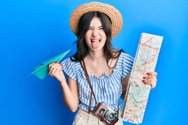 Elinde kağıt uçak ve şehir haritası olan güzel beyaz bir kız komik bir ifadeyle dilini dışarı çıkarıyor.. 