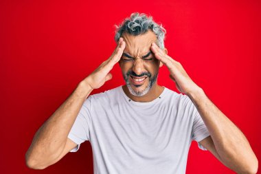 Orta yaşlı, gri saçlı, günlük beyaz tişört giyen baş ağrısı çeken çaresiz ve stresli bir adam. Ağrı ve migren yüzünden. Eller başının üstünde.. 