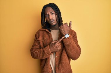 Kahverengi retro ceketli Afrikalı Amerikalı adam acele ederek saati, sabırsızlığı ve rahat bir ifadeyle kameraya bakıyor. 