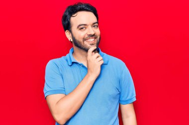 Gündelik giysiler giyen genç İspanyol adam kameraya kollarını kavuşturup çenesine dokunarak gülümsüyor. Olumlu düşünmek. 