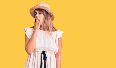 Yaz şapkası ve tişörtü giyen genç ve güzel bir kadın ağzıyla ağzını kapatmaktan sıkılmış. Huzursuz ve uykulu.. 