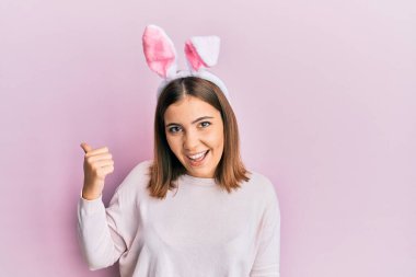 Sevimli paskalya tavşanı kulakları takan neşeli yüzüyle gülümseyen ve başparmağıyla yan tarafı gösteren güzel bir kadın.. 
