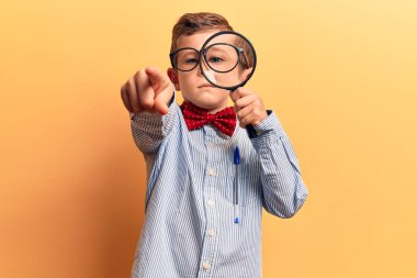 Sevimli sarışın çocuk inek papyonu takıyor ve elinde büyüteçle kamerayı işaret ediyor. Kendine güvenen ve ciddi görünen bir jest. 