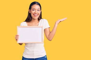 Genç ve güzel Latin kız elinde boş beyaz karatahta ile zaferi kutluyor mutlu bir gülümseme ve ellerini kaldırarak kazanan ifade. 