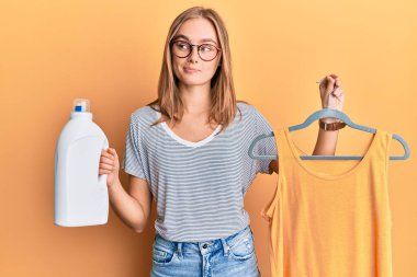 Askıda tişört tutan güzel sarışın kadın ve deterjan şişesi gülümsüyor yan bakıyor ve düşünüyor.. 