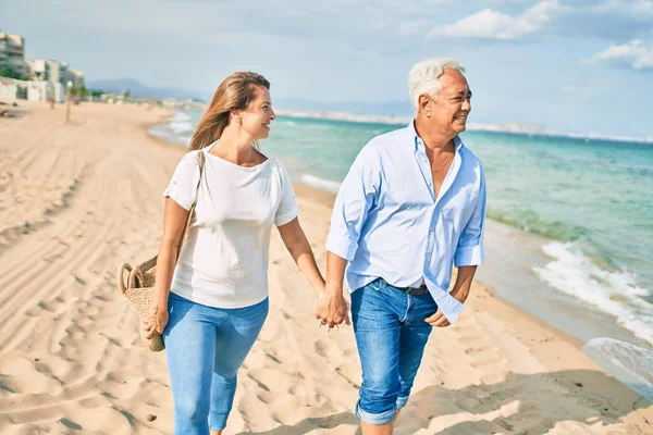 Orta yaşlı İspanyol çift kumsalda yürürken mutlu bir şekilde gülümsüyor..