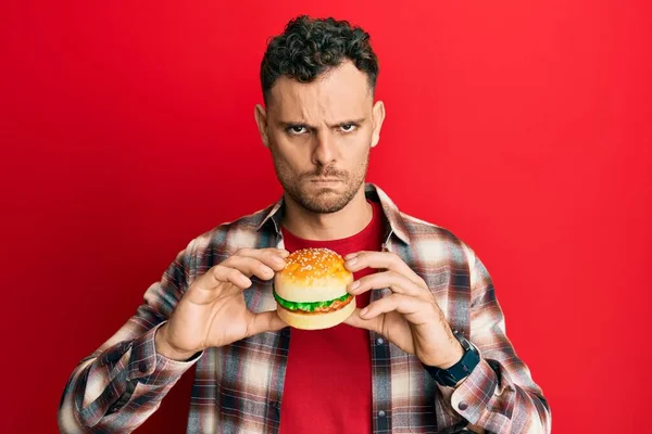 Young Hispanic Man Eating Tasty Classic Burger Skeptic Nervous Frowning — Stock Photo, Image