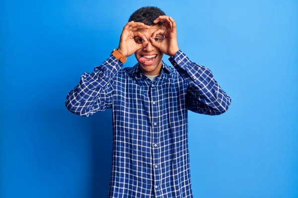 若いアフリカ系アメリカ人の男性がカジュアルな服を着て 双眼鏡の舌を突き出すようなOkジェスチャーをして 目を指で見ている クレイジーな表現 — ストック写真