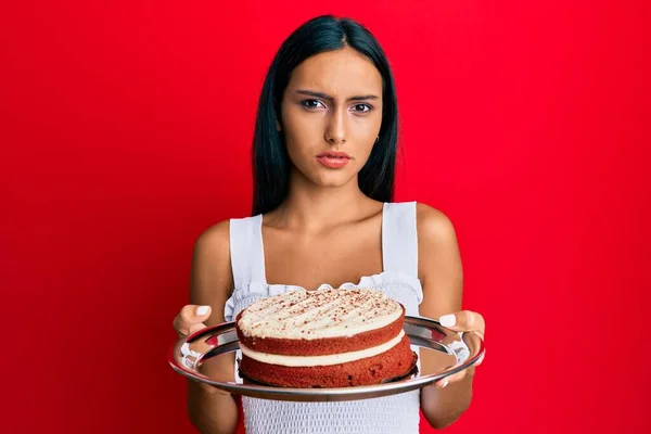 ニンジンケーキを持っている若いブルネットの女性は無知で混乱した表情 疑わしい概念 — ストック写真