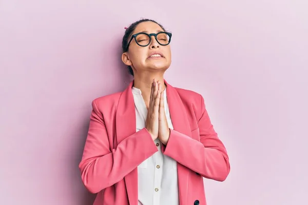 Beautiful middle eastern woman wearing business jacket and glasses begging and praying with hands together with hope expression on face very emotional and worried. begging.