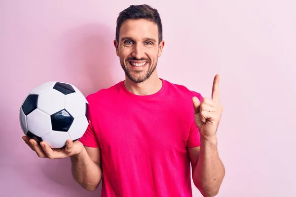 잘생긴 선수가 분홍색 위에서 축구공을 손가락으로 가리키며 행복하게 — 스톡 사진