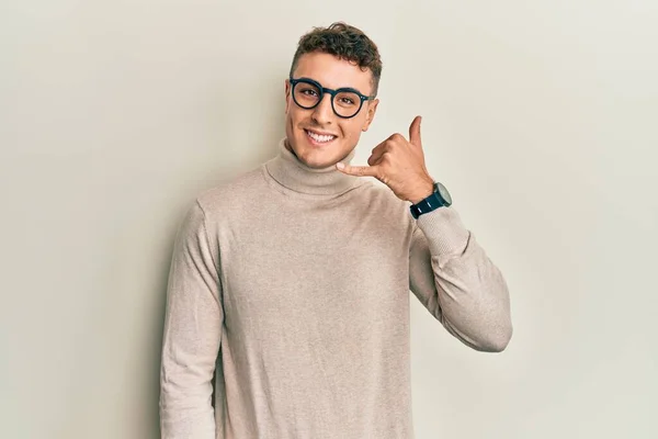 스페인 청년은 터틀넥 스웨터를 손가락으로 통화를 것처럼 미소를 — 스톡 사진