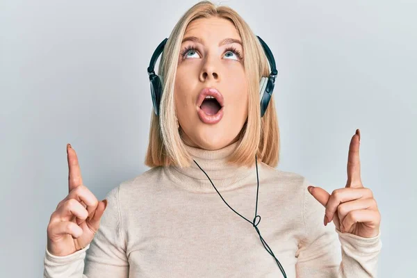 Νεαρή Ξανθιά Γυναίκα Ακούγοντας Μουσική Χρησιμοποιώντας Ακουστικά Κατάπληκτος Και Έκπληκτος — Φωτογραφία Αρχείου