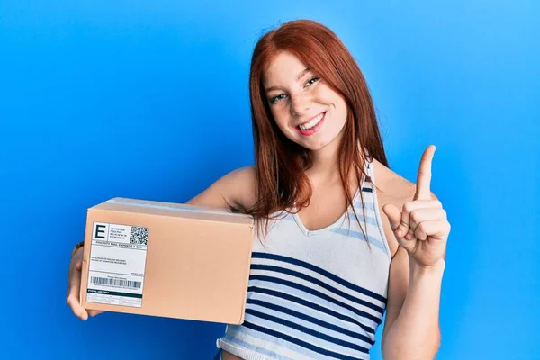 Young Red Head Girl Holding Delivery Package Smiling Idea Question — Stock Photo, Image