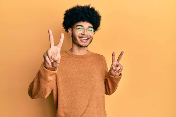 年轻的非洲裔美国人 头发是非洲裔 穿着休闲的冬季毛衣 微笑着看着摄像机 手指头在做胜利的标志 第二点 — 图库照片