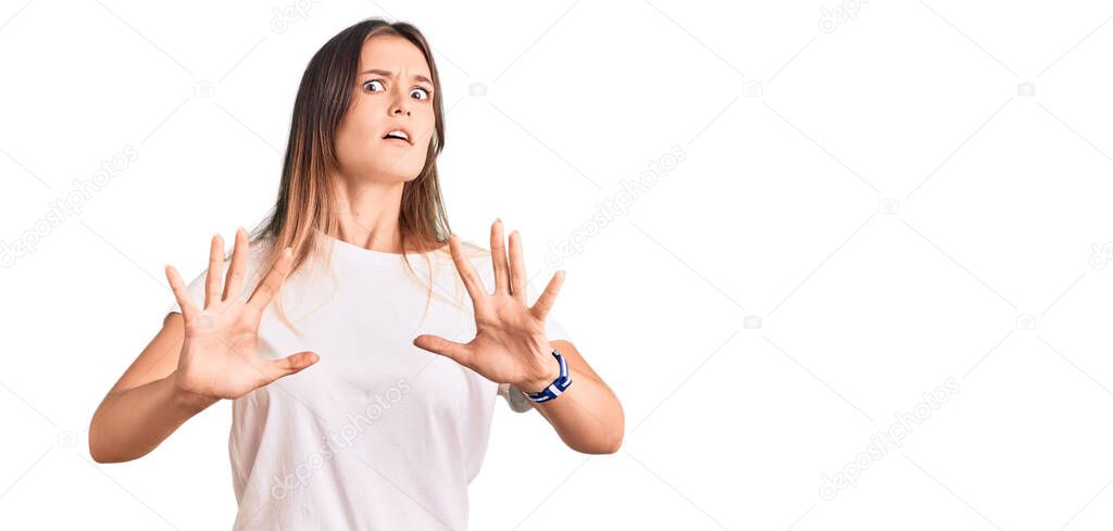 Beautiful caucasian woman wearing casual white tshirt afraid and terrified with fear expression stop gesture with hands, shouting in shock. panic concept. 