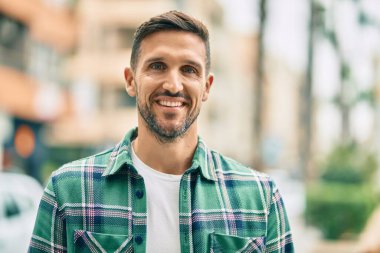 Genç beyaz adam gülümseyerek şehirde mutlu mesut duruyor..