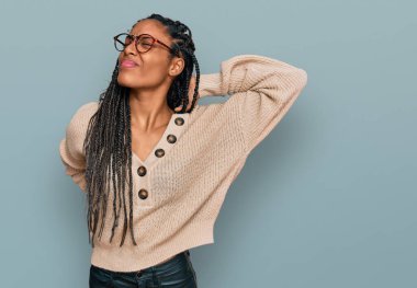 Sıradan kıyafetler giyen Afrikalı Amerikalı kadın boyun ağrısı çekiyor, elle boyuna dokunuyor, kas ağrısı çekiyor. 