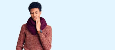 Genç Afro-Amerikan erkek, diş ağrısı ya da diş ağrısı yüzünden sıradan bir kazak ve eşarp giyer ve ağzına acı dolu bir ifadeyle dokunur. dişçi 