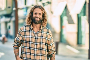 Uzun saçlı beyaz bir adam şehirde mutlu bir şekilde gülümsüyor..