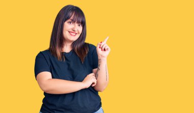 Genç ve cüsseli bir kadın. Günlük kıyafetler giyiyor. Yüzünde kocaman bir gülümseme var. Elleri ve parmakları kameraya bakıyor.. 