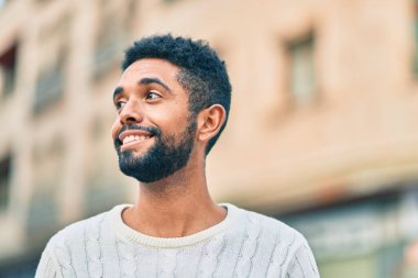 Genç Afrikalı Amerikalı adam gülümseyerek şehirde mutlu mesut duruyor..