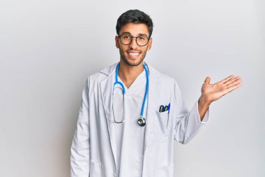Doktor üniforması ve steteskop giyen genç yakışıklı adam mutlu bir şekilde gülümsüyor ve avuç içi kameraya bakıyor.. 