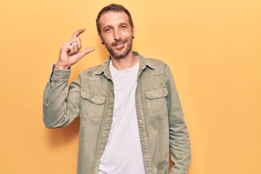 Gündelik kıyafetler giyen, gülümseyen, kendine güvenen, el hareketleriyle küçük boy işareti yapan, parmaklarıyla işaret eden ve kameraya bakan genç yakışıklı bir adam. ölçüm kavramı. 