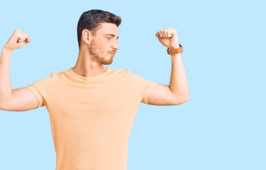 Sarı bir tişört giyen yakışıklı genç adam gururla gülümseyen kol kaslarını gösteriyor. fitness konsepti. 