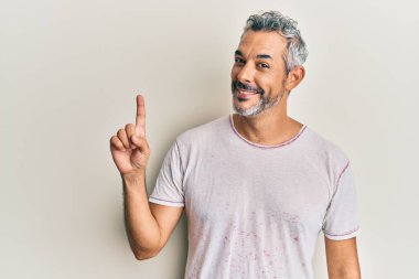 Orta yaşlı, gri saçlı, günlük kıyafetler giyen bir numaralı parmağı gösteren ve gülümseyen, kendinden emin ve mutlu bir adam.. 