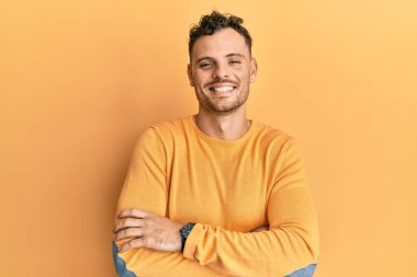 Gündelik kıyafetler giyen, kollarını kavuşturup kameraya gülümseyen genç İspanyol adam. pozitif kişi. 