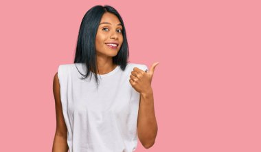 Genç Afro-Amerikan kadın, günlük kıyafetler giyip gülümsüyor, gülümsüyor ve başparmağıyla yan tarafı işaret ediyor.. 