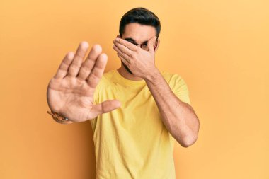 Gündelik kıyafetler giyen, gözlüklü, elleriyle gözlerini kapatan, üzgün ve korku ifadeleriyle jest yapan genç bir İspanyol. utangaç ve olumsuz kavram. 