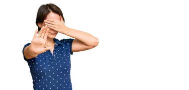 Kısa saçlı, esmer, sıradan kıyafetler giyen, elleriyle gözleri kapayan, üzgün ve korku dolu hareketler yapan genç bir kadın. utangaç ve olumsuz kavram. 