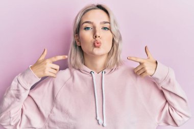 Güzel ve seksi bir şekilde öpüşürken parmaklarıyla kameraya bakan genç sarışın kız. aşk ifadesi. 