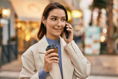 Genç İspanyol kadın gülümsüyor. Şehirdeki akıllı telefondan konuşuyor..