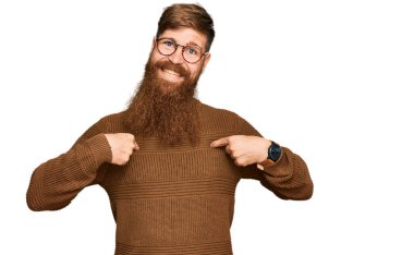 Genç İrlandalı kızıl saçlı, günlük kıyafetler ve gözlük takan, kendine güvenen, gülümseyen, kendini gururlu ve mutlu parmaklarıyla gösteren bir adam.. 